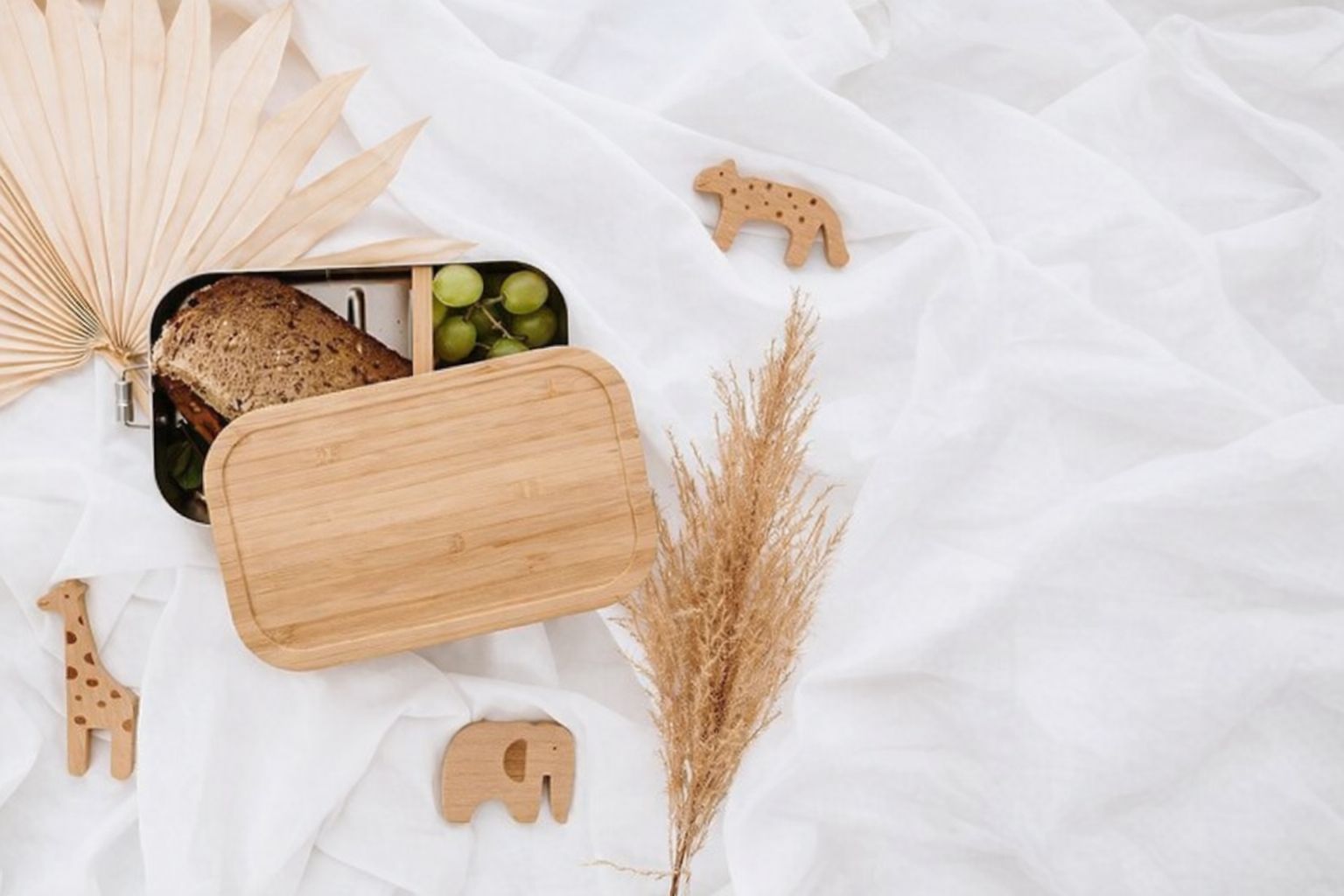 Matlåda med smörgås, vindruvor och träleksaker på vitt tyg.